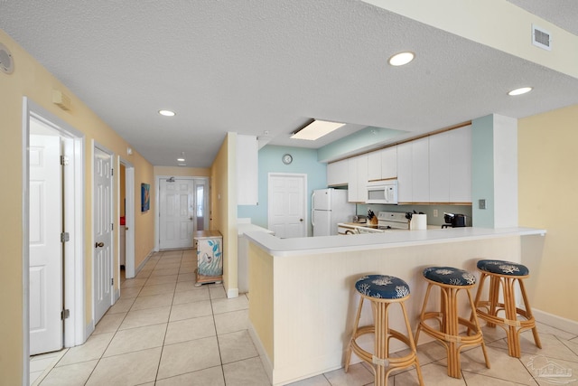 kitchen featuring white cabinets, white appliances, a breakfast bar, kitchen peninsula, and a textured ceiling