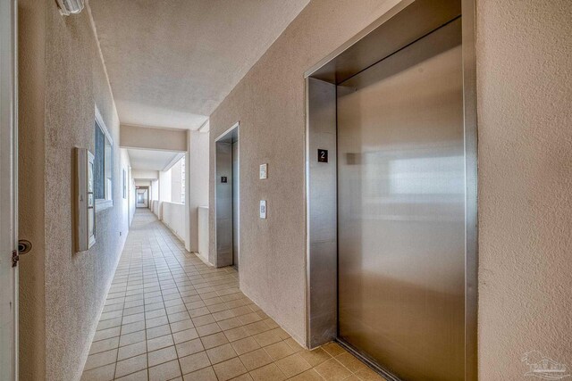 hallway with light tile patterned floors, elevator, and a textured ceiling