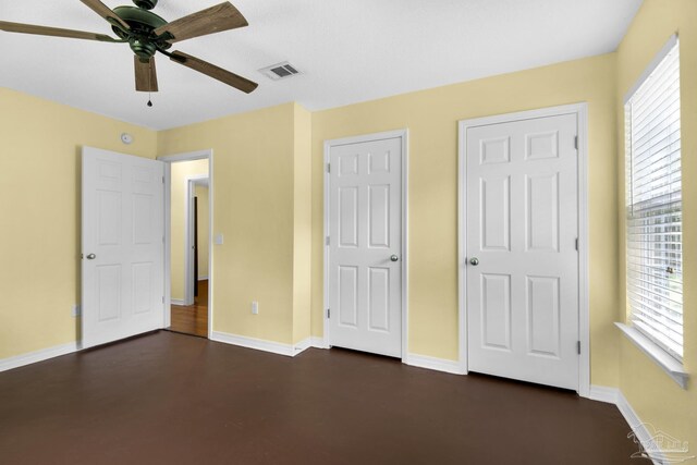 unfurnished bedroom with two closets, dark hardwood / wood-style flooring, multiple windows, and ceiling fan