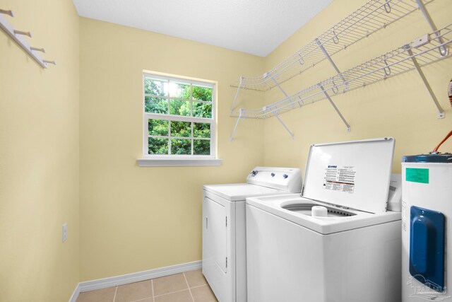 laundry area with electric water heater, washing machine and dryer, and light tile patterned flooring