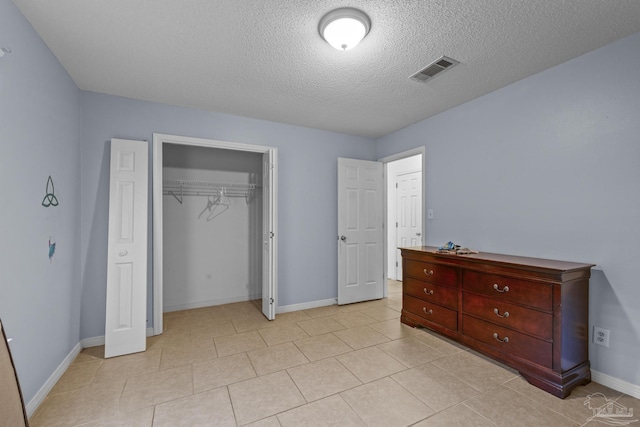 bedroom featuring visible vents, a textured ceiling, a closet, light tile patterned floors, and baseboards