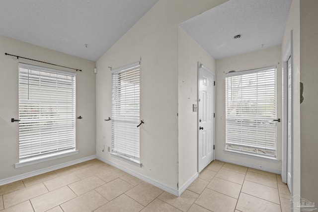 foyer entrance featuring light tile patterned floors, lofted ceiling, a textured ceiling, and a wealth of natural light