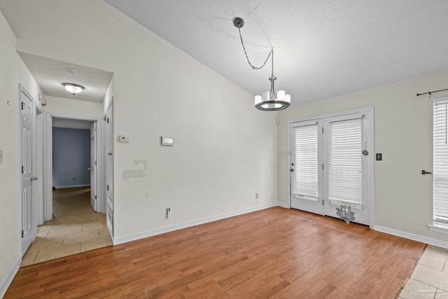 unfurnished dining area with a chandelier, light wood-type flooring, baseboards, and vaulted ceiling