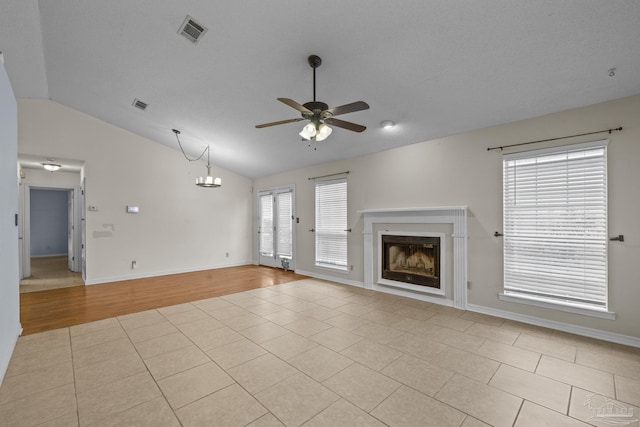 unfurnished living room featuring visible vents, vaulted ceiling, ceiling fan with notable chandelier, a fireplace, and light tile patterned flooring