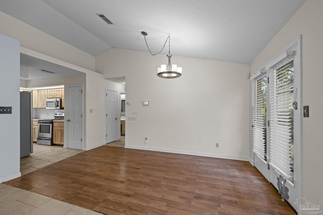 interior space featuring visible vents, baseboards, lofted ceiling, an inviting chandelier, and wood finished floors