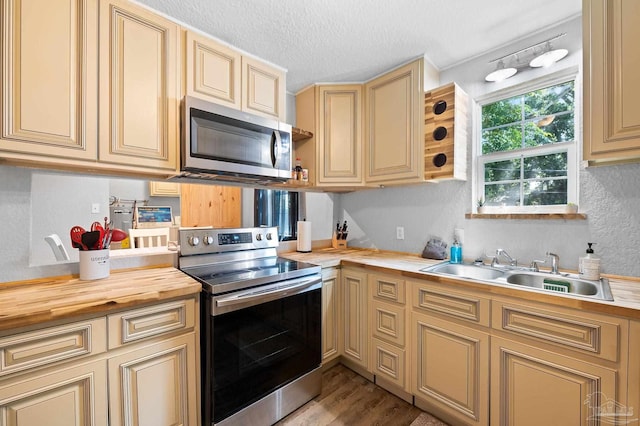 kitchen with wood counters, appliances with stainless steel finishes, a textured ceiling, sink, and light hardwood / wood-style floors