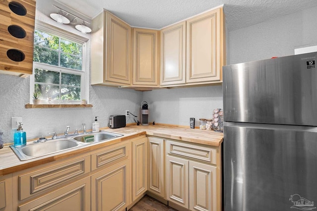 kitchen with stainless steel fridge, a textured ceiling, butcher block countertops, and sink