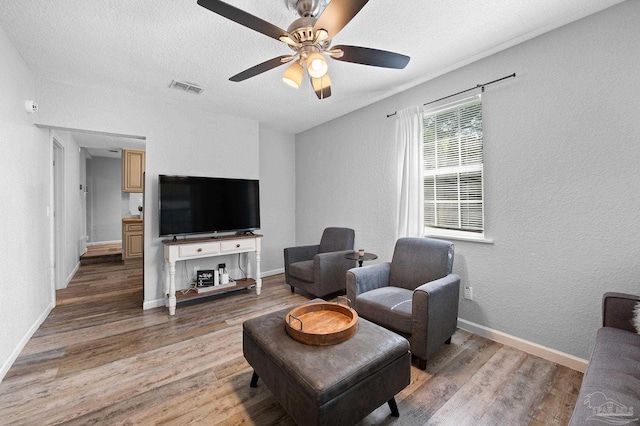 living room with ceiling fan, a textured ceiling, and light wood-type flooring