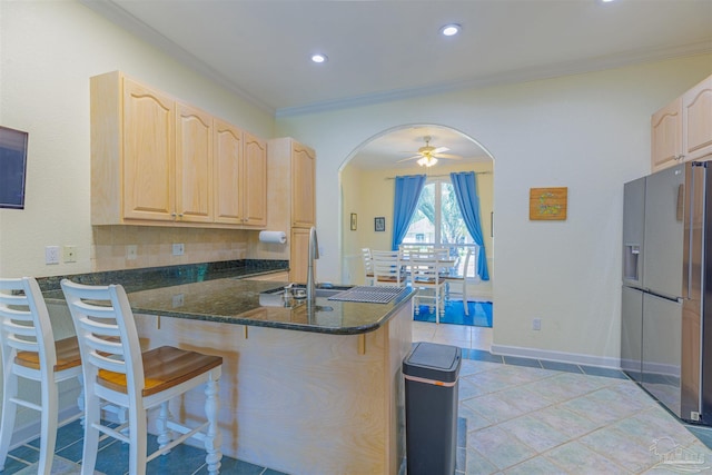 kitchen with kitchen peninsula, dark stone countertops, crown molding, and stainless steel refrigerator with ice dispenser