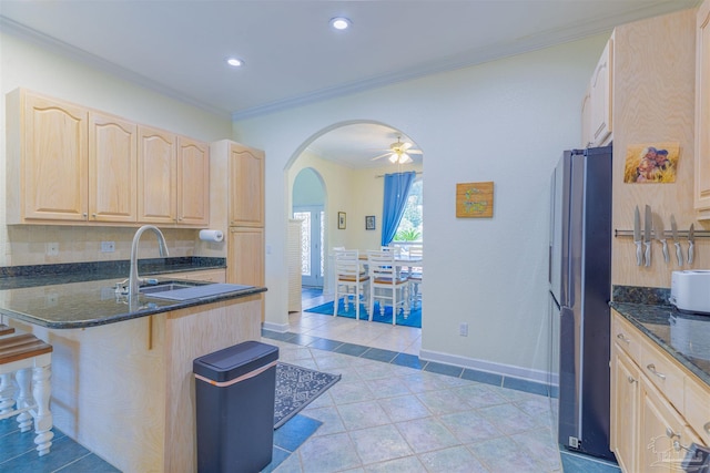 kitchen featuring sink, dark stone counters, ornamental molding, and stainless steel refrigerator