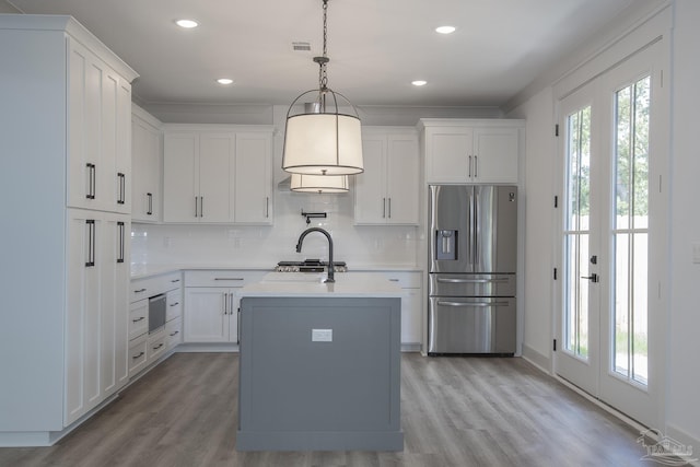 kitchen with appliances with stainless steel finishes, a kitchen island with sink, hanging light fixtures, and white cabinets