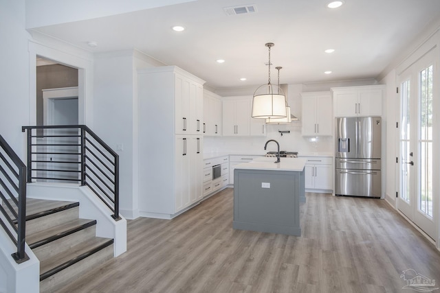 kitchen featuring white cabinetry, hanging light fixtures, light hardwood / wood-style flooring, stainless steel fridge, and a kitchen island with sink