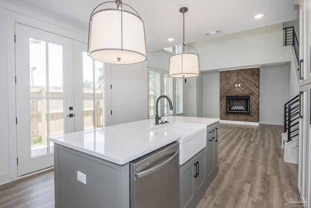 kitchen with decorative light fixtures, sink, gray cabinetry, stainless steel dishwasher, and a center island with sink