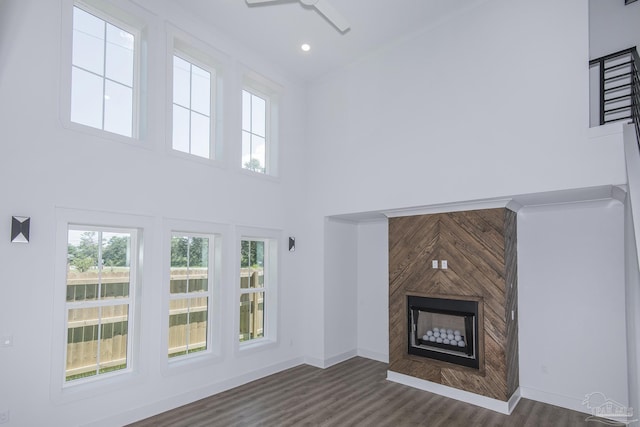 unfurnished living room featuring ceiling fan, a large fireplace, dark hardwood / wood-style flooring, and a high ceiling