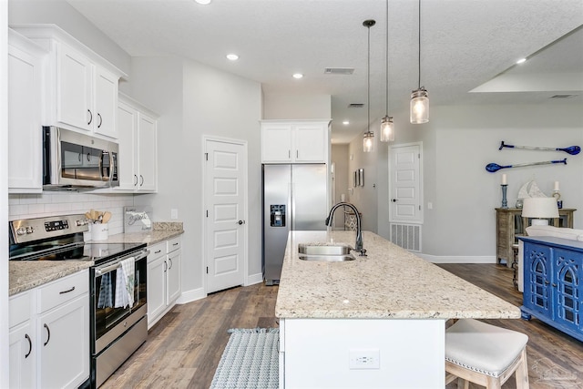 kitchen with pendant lighting, appliances with stainless steel finishes, a kitchen island with sink, a sink, and white cabinetry