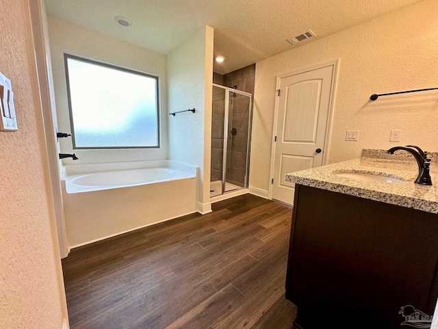 bathroom with a shower stall, wood finished floors, a textured wall, a garden tub, and vanity