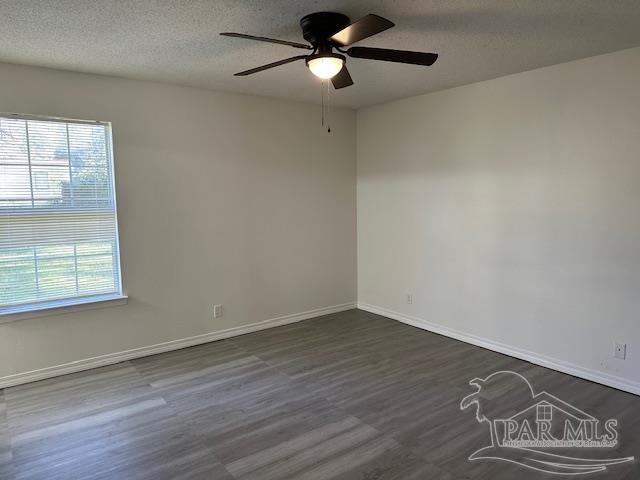 empty room with a textured ceiling, dark wood-type flooring, baseboards, and a ceiling fan