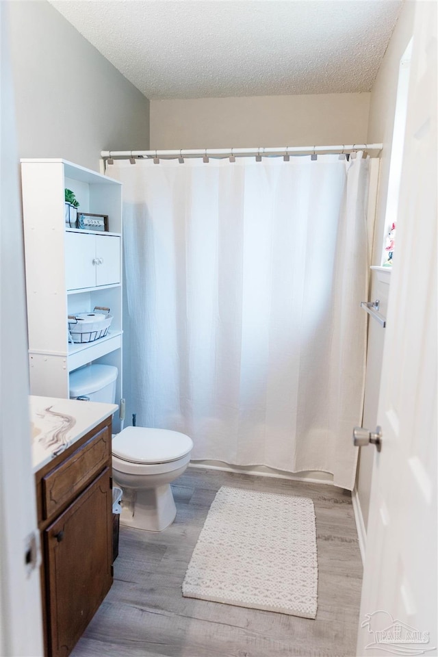 bathroom featuring wood finished floors, a textured ceiling, toilet, vanity, and a shower with curtain
