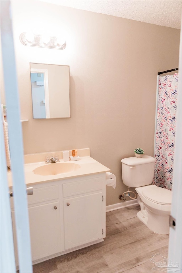bathroom with toilet, wood finished floors, vanity, baseboards, and a shower with curtain