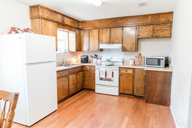 kitchen with white appliances, a sink, under cabinet range hood, and brown cabinetry