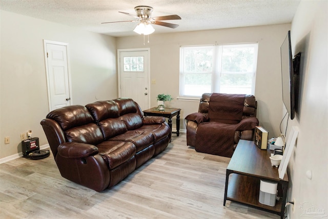 living area featuring a ceiling fan, light wood-type flooring, baseboards, and a textured ceiling