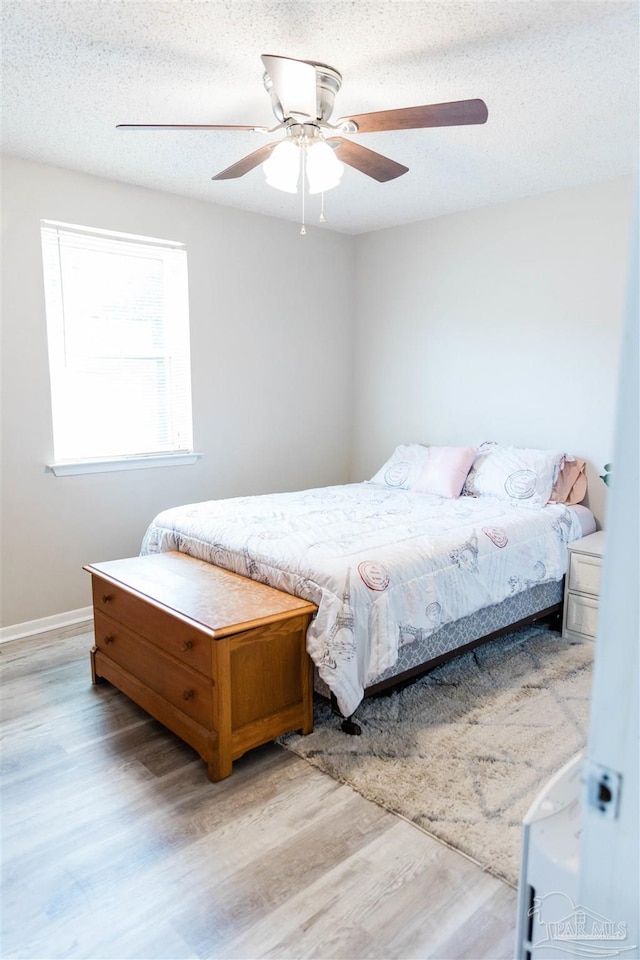 bedroom with light wood-style floors, a ceiling fan, baseboards, and a textured ceiling