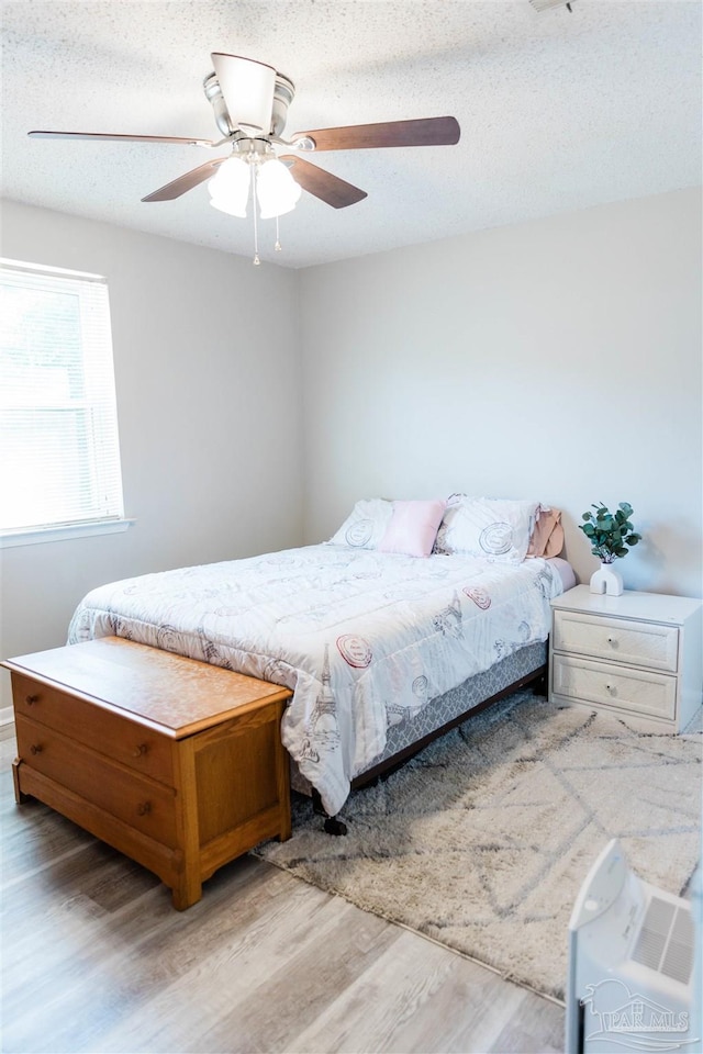 bedroom featuring light wood finished floors, a ceiling fan, and a textured ceiling