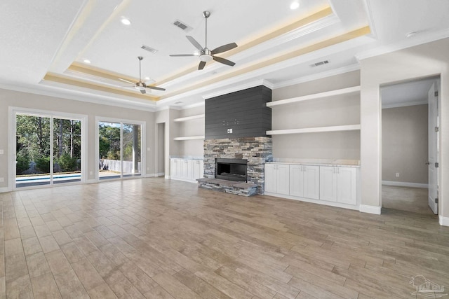 unfurnished living room with built in shelves, a stone fireplace, ornamental molding, and a tray ceiling