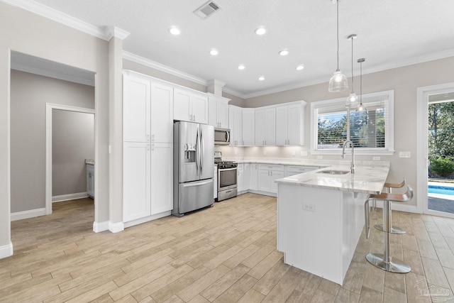 kitchen with sink, appliances with stainless steel finishes, decorative light fixtures, white cabinetry, and a breakfast bar area