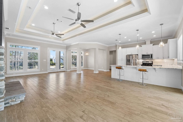 unfurnished living room with light wood-type flooring, a raised ceiling, ceiling fan, and crown molding