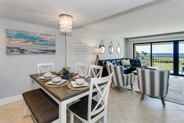 dining space with light tile patterned floors, wood walls, a water view, and an inviting chandelier