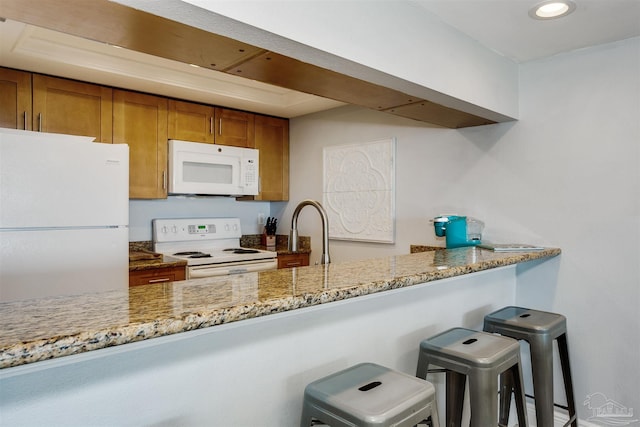 kitchen with light stone counters, sink, white appliances, and a breakfast bar area