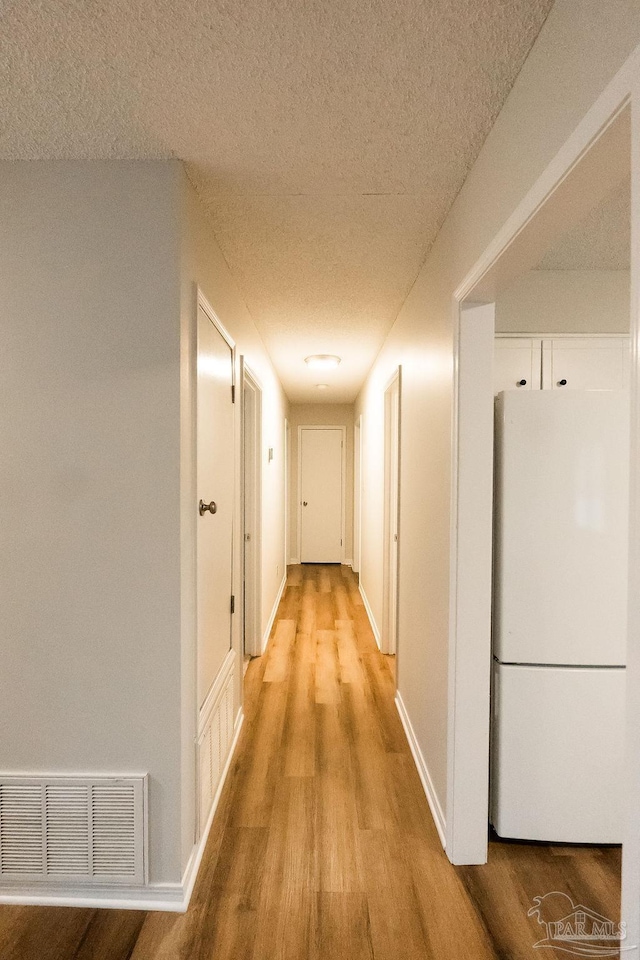 corridor featuring a textured ceiling, light wood-style flooring, visible vents, and baseboards