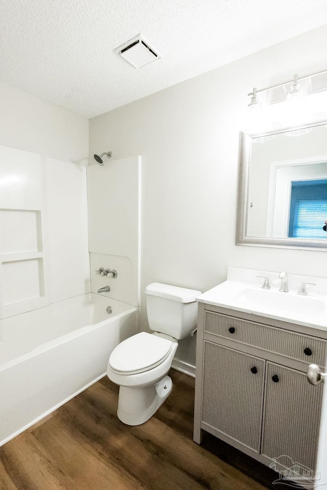 bathroom with a textured ceiling, toilet, wood finished floors, vanity, and tub / shower combination