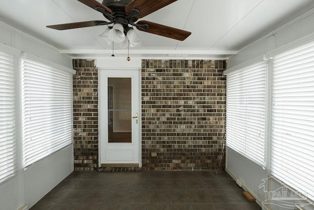 spare room featuring a ceiling fan, dark tile patterned floors, and brick wall