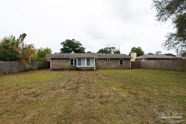 rear view of property with a fenced backyard, a yard, and brick siding