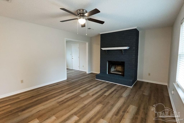 unfurnished living room with a textured ceiling, dark hardwood / wood-style floors, a brick fireplace, and ceiling fan