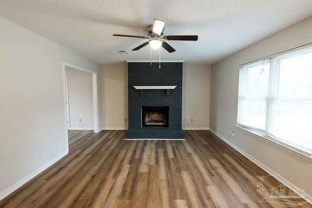 unfurnished living room featuring a fireplace, a textured ceiling, baseboards, and wood finished floors