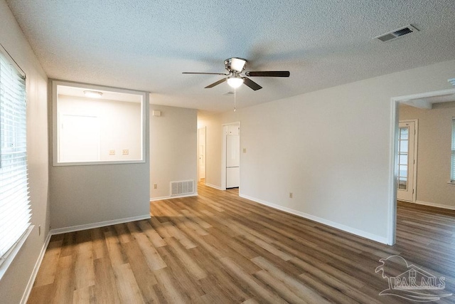 spare room featuring visible vents, a textured ceiling, baseboards, and wood finished floors