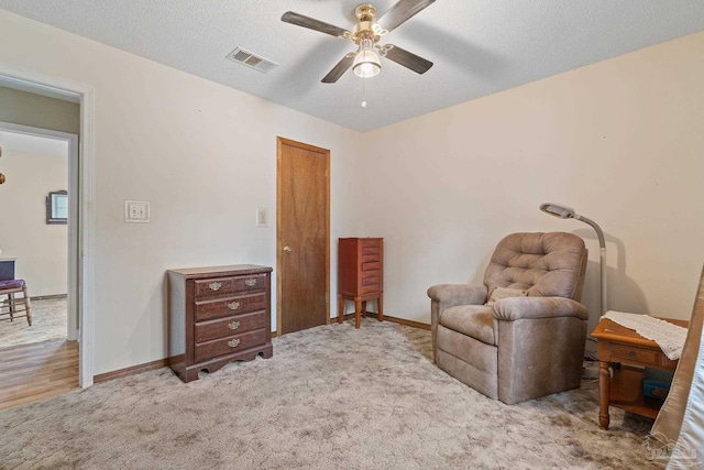 living area with a textured ceiling, light colored carpet, and ceiling fan