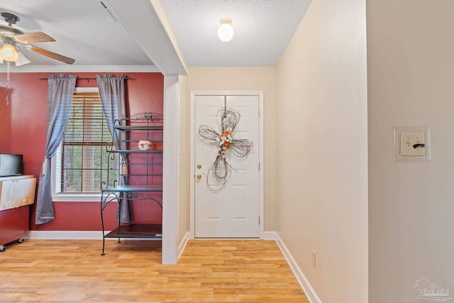 foyer entrance with ceiling fan, light hardwood / wood-style floors, a textured ceiling, and ornamental molding