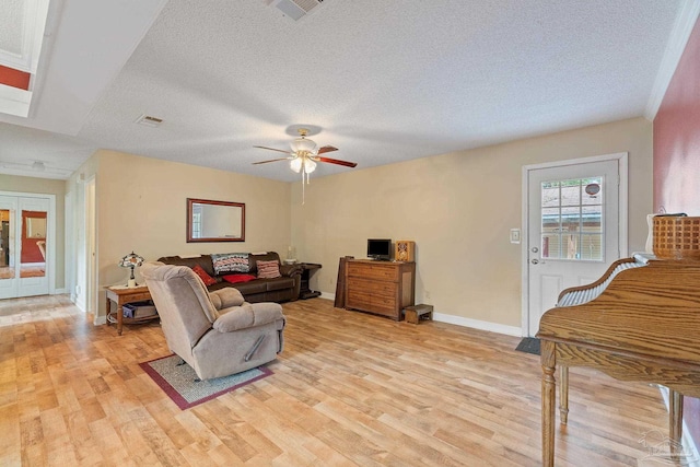 living room featuring ceiling fan, light wood-type flooring, and a textured ceiling