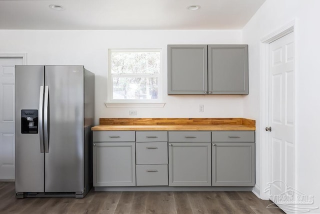 kitchen with stainless steel refrigerator with ice dispenser, dark wood-type flooring, wooden counters, and gray cabinets