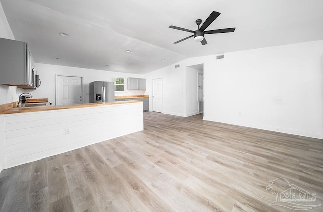 unfurnished living room featuring ceiling fan, vaulted ceiling, sink, and light hardwood / wood-style floors