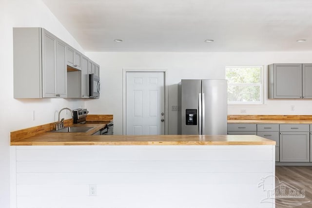 kitchen featuring gray cabinetry, hardwood / wood-style floors, butcher block counters, stainless steel appliances, and kitchen peninsula