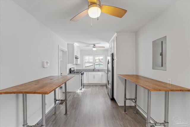 kitchen featuring a kitchen bar, appliances with stainless steel finishes, electric panel, hardwood / wood-style floors, and white cabinets