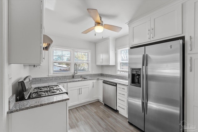 kitchen featuring appliances with stainless steel finishes, white cabinetry, sink, light stone countertops, and light hardwood / wood-style flooring