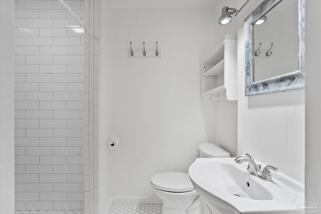 bathroom with tile patterned flooring, sink, toilet, and tiled shower