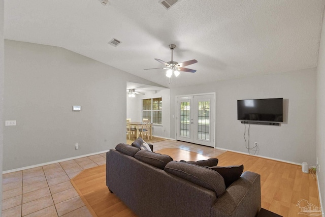 living room featuring french doors, vaulted ceiling, ceiling fan, a textured ceiling, and light hardwood / wood-style floors