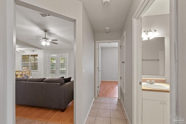 corridor with sink, a textured ceiling, and light wood-type flooring